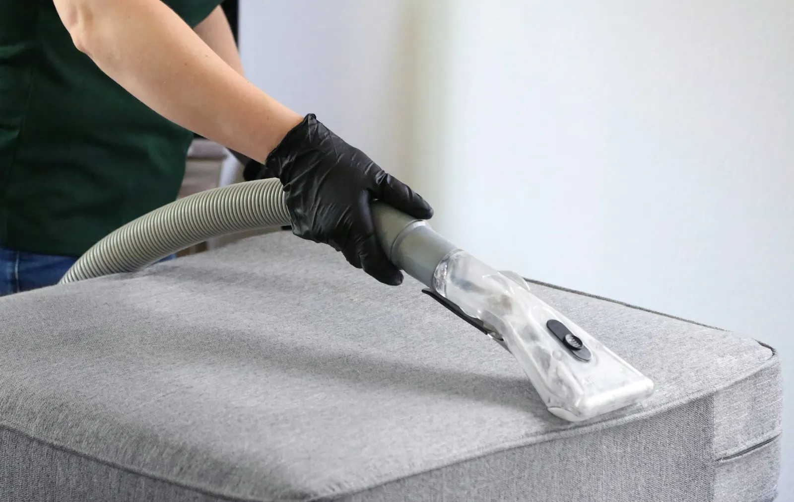 Hand in Handschuh reinigt ein graues Polsterkissen mit der Düse eines Sprühextraktionsgeräts