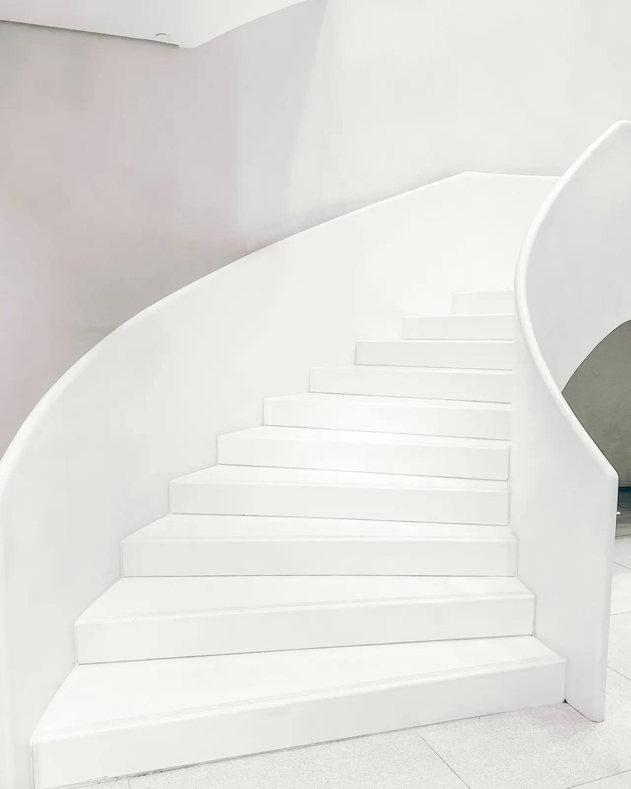 Geschwungene, strahlend weiße Treppe in einem hellen Innenraum